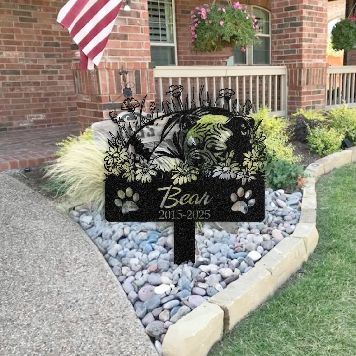 American Bully pet grave marker placed in a rock garden bed in front of a brick house porch with an American flag