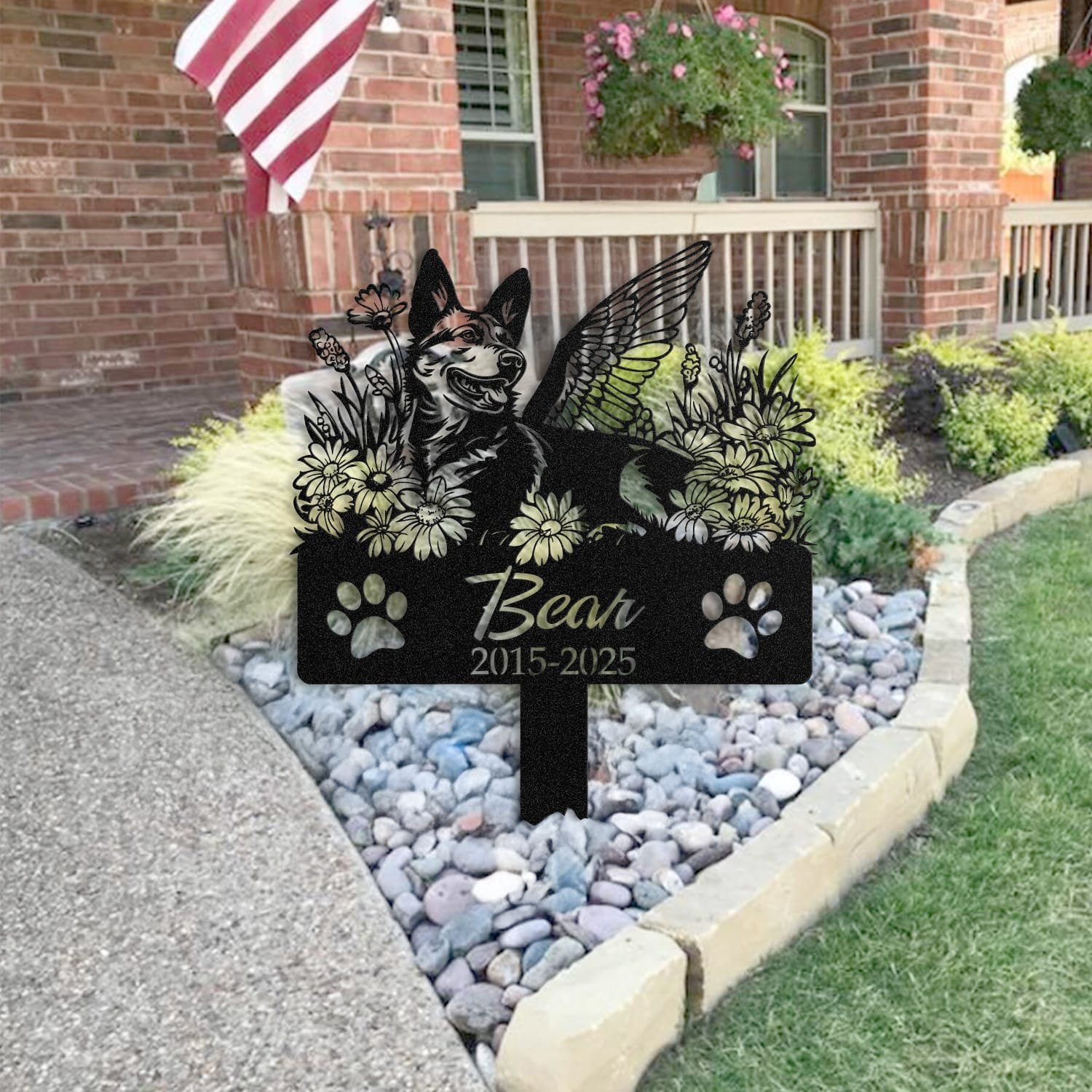 Australian Cattle Dog pet grave marker placed in a rock garden bed in front of a brick house porch with an American flag