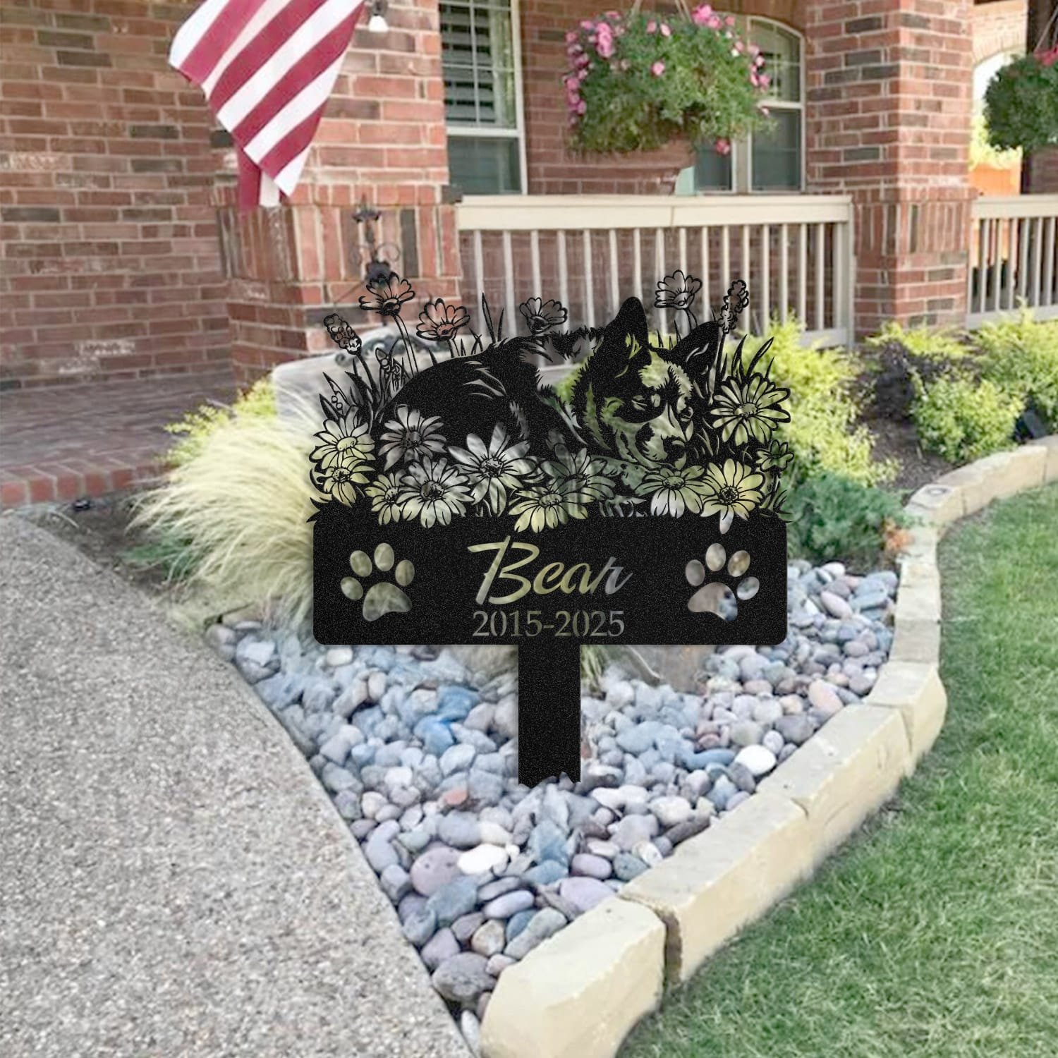 Australian Cattle Dog pet grave marker placed in a rock garden bed in front of a brick house porch with an American flag