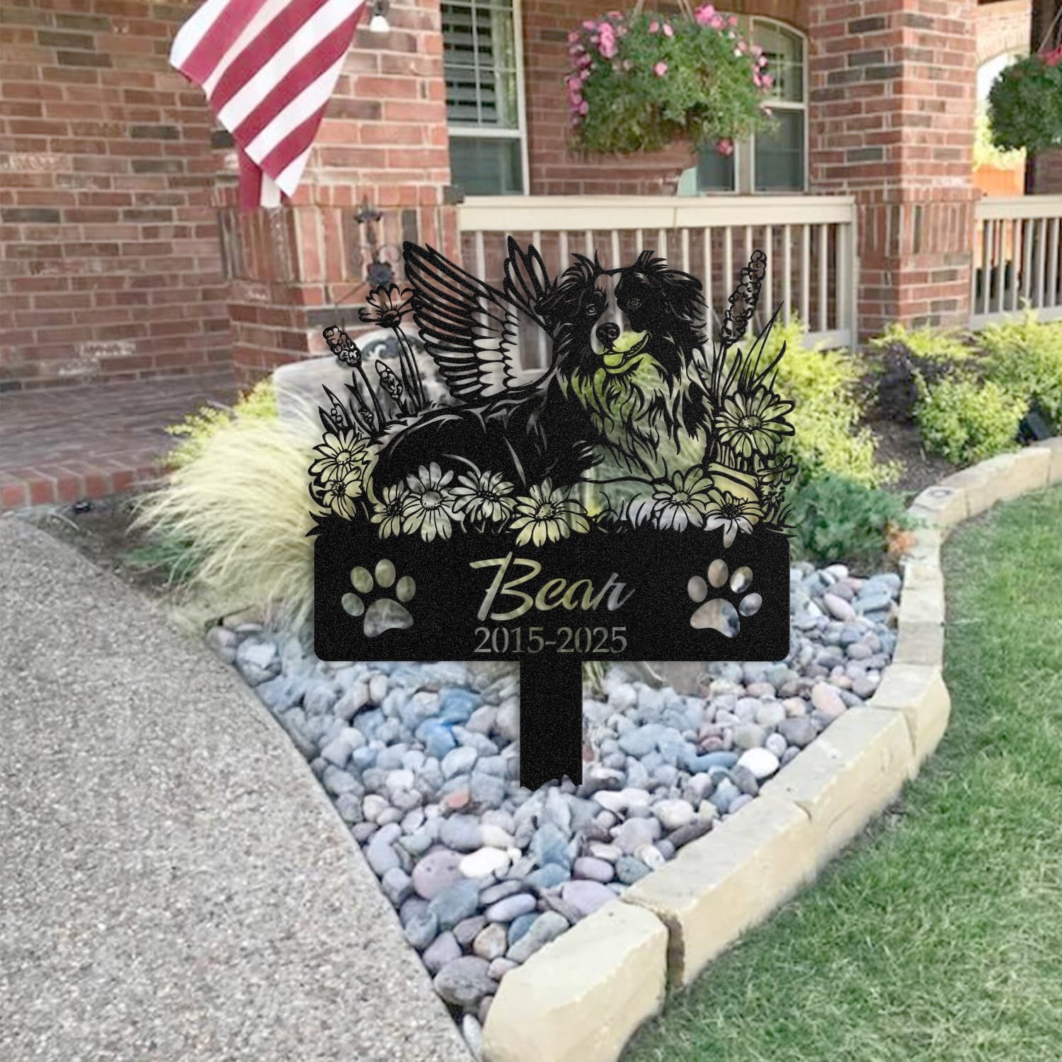 Australian Shepherd pet grave marker placed in a rock garden bed in front of a brick house porch with an American flag