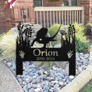 Personalized Bearded Dragon metal pet grave marker with a heart cutout, displayed in a rock garden bed in front of a brick house porch with an American flag