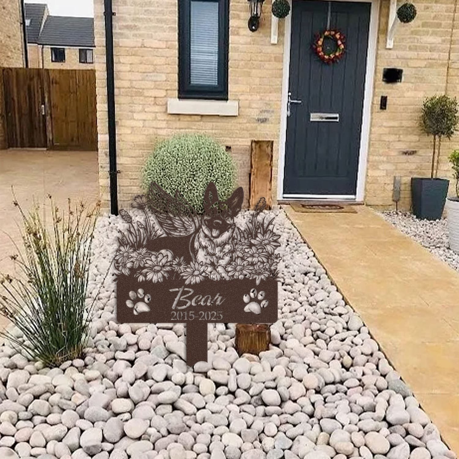 Belgian Malinois pet grave marker in a light stone garden bed outside a brick home with a blue front door and wreath