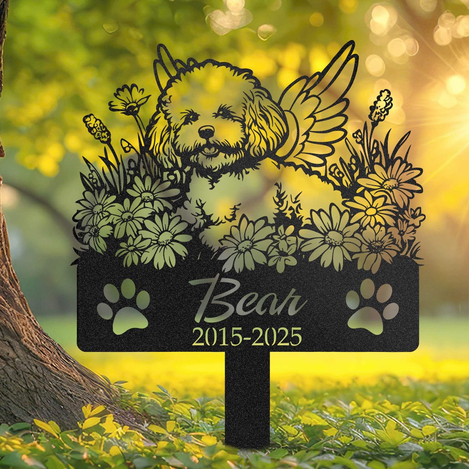 Bichon Frise angel wings pet grave marker staked into the ground beside a large tree trunk in a garden setting