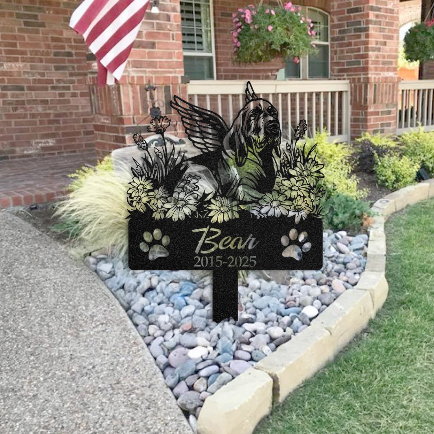 Bloodhound pet grave marker placed in a rock garden bed in front of a brick house porch with an American flag
