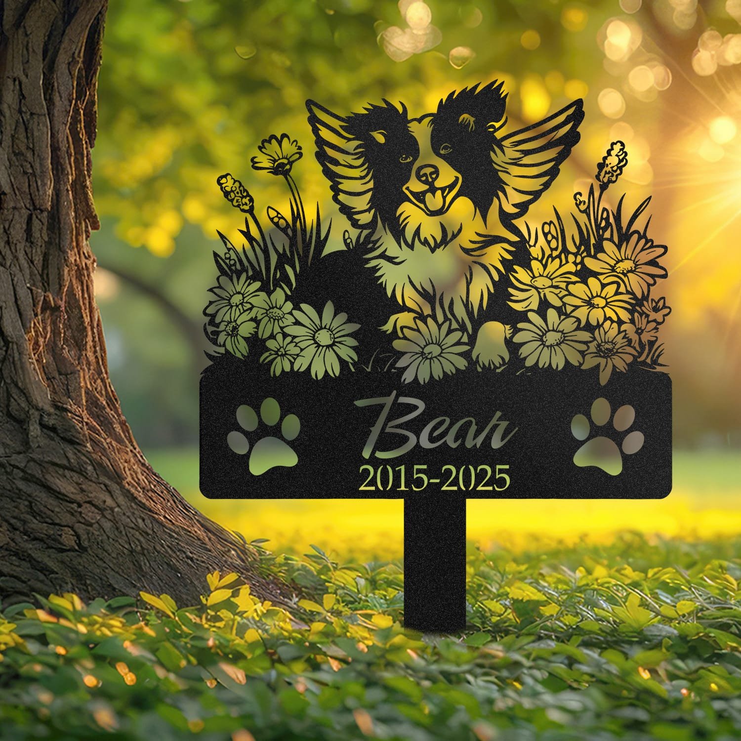 Border Collie angel wings pet grave marker staked into the ground beside a large tree trunk in a garden setting