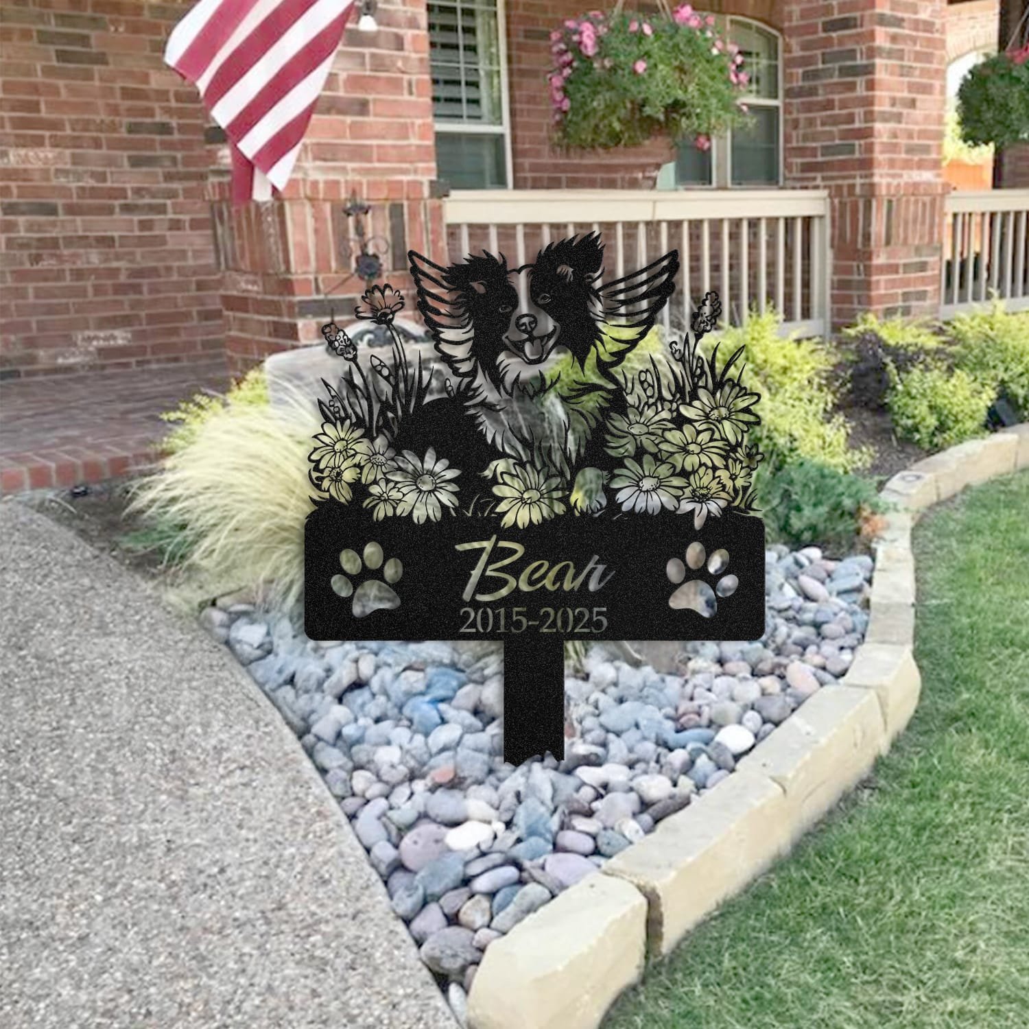 Border Collie pet grave marker placed in a rock garden bed in front of a brick house porch with an American flag