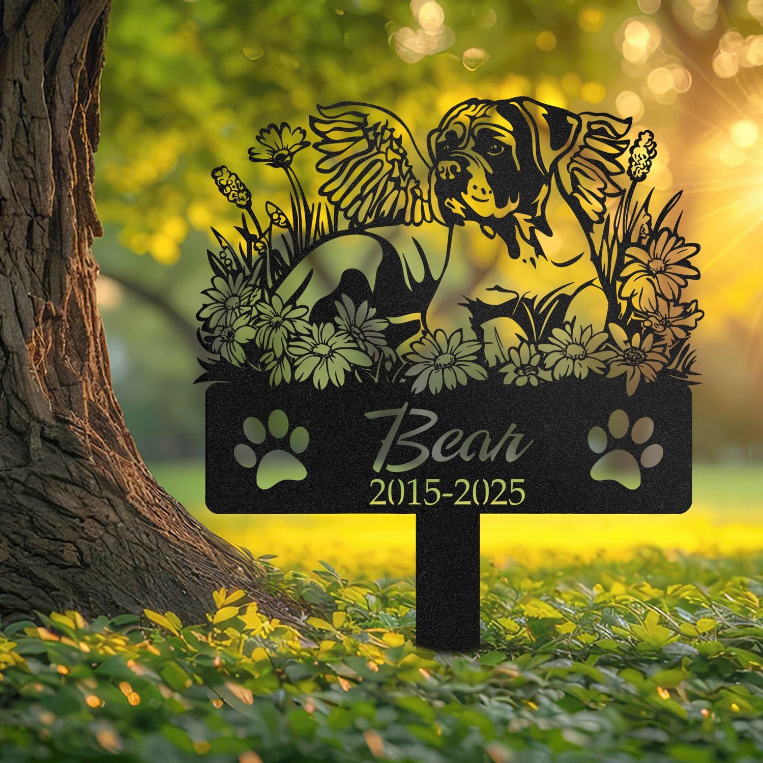 Boxer angel wings pet grave marker staked into the ground beside a large tree trunk in a garden setting