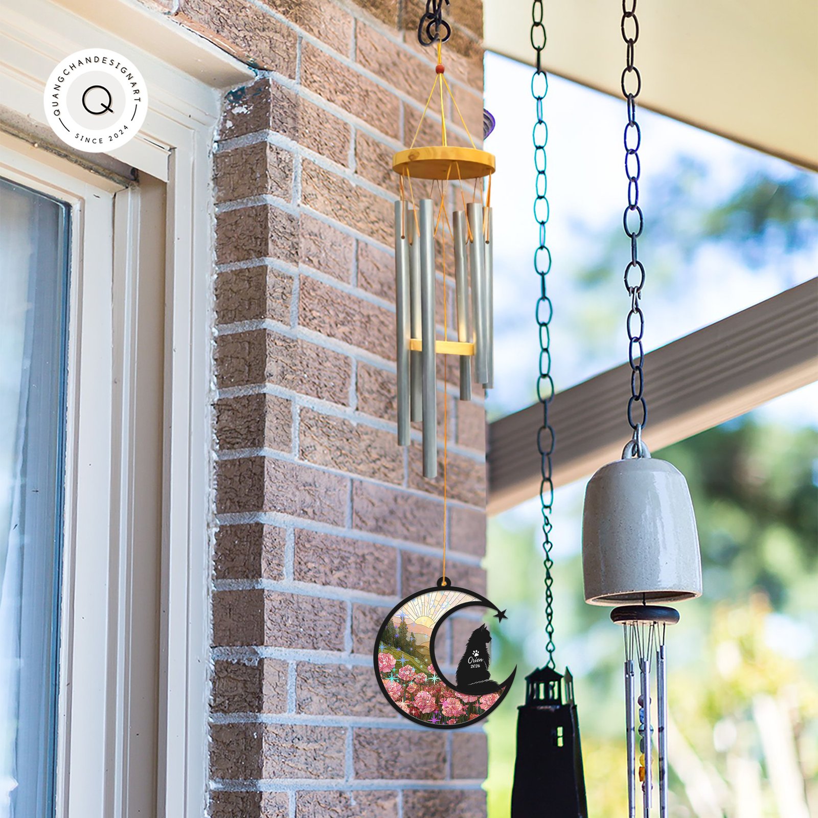 Wind chime with a Long-Haired Cat memorial suncatcher hanging outdoors near a brick wall alongside other garden bells and chimes