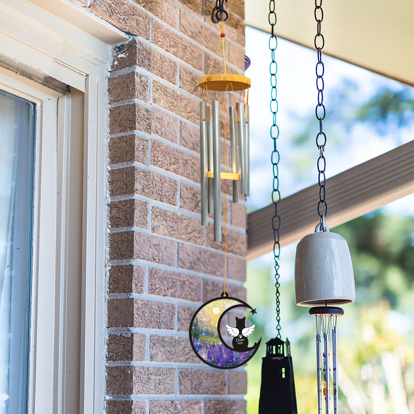 Short-haired cat wind chime suncatcher hanging outdoors near a brick wall alongside other decorative bells and chimes