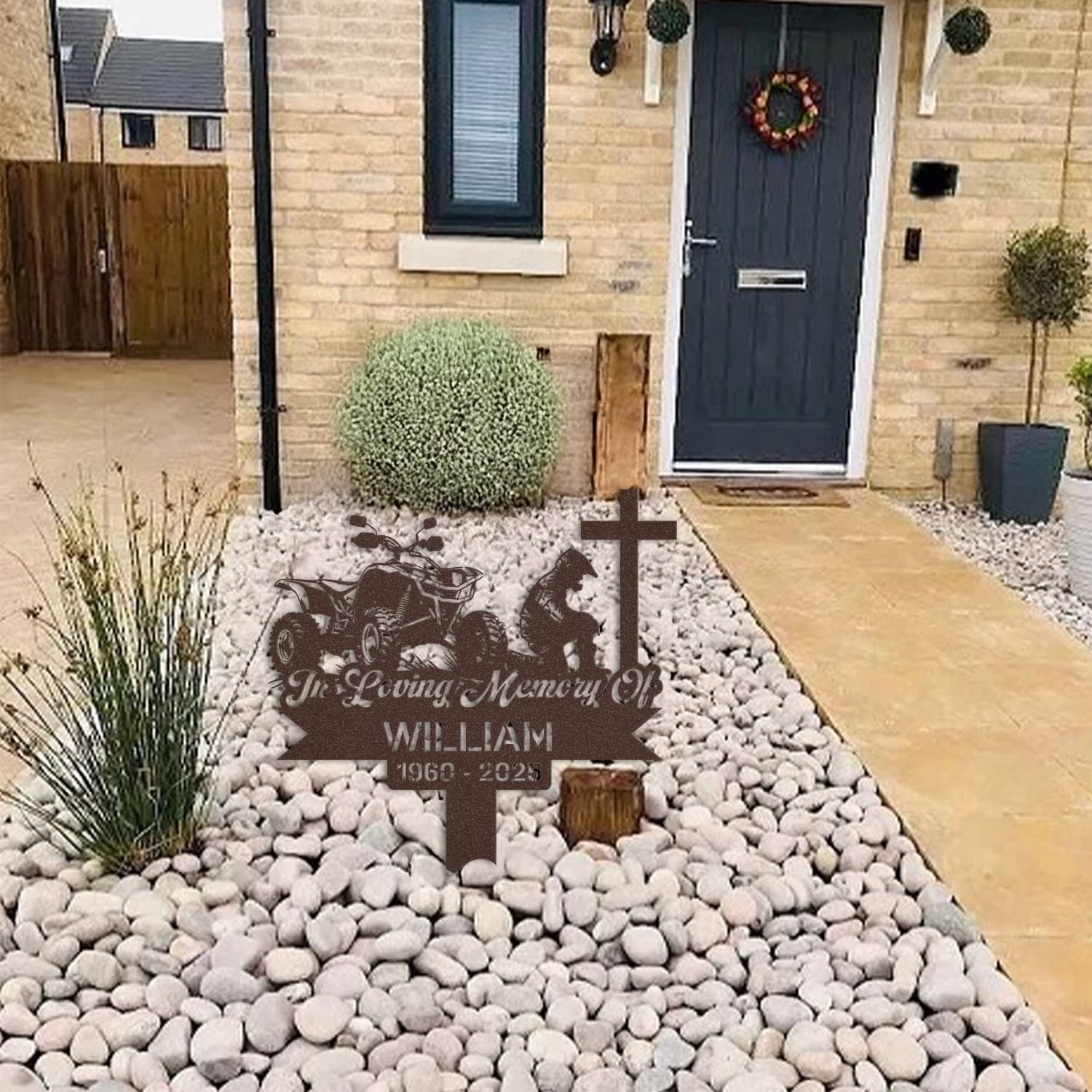 ATV human grave marker displayed among garden plants and stone edging, showing the atv kneeling-at-the-cross design as an outdoor memorial accent.