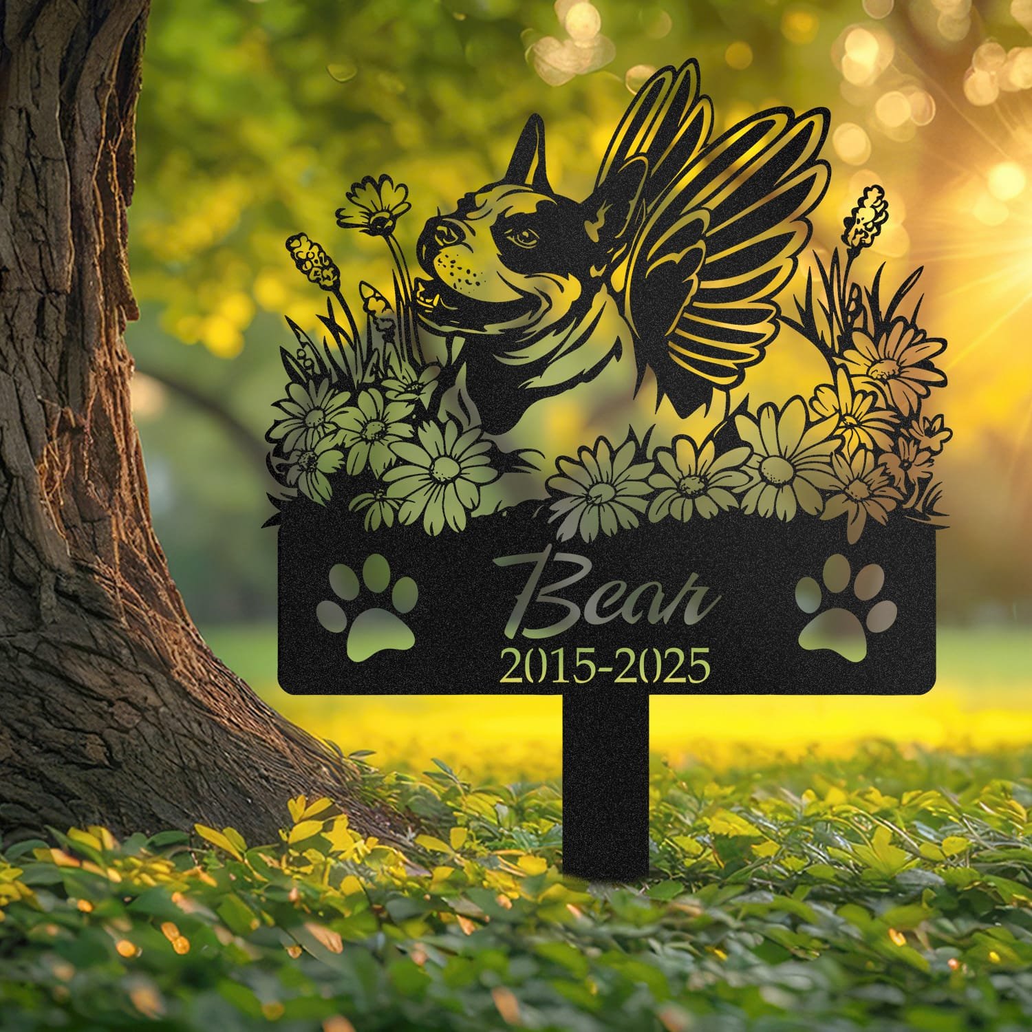 Bull Terrier angel wings pet grave marker staked into the ground beside a large tree trunk in a garden setting