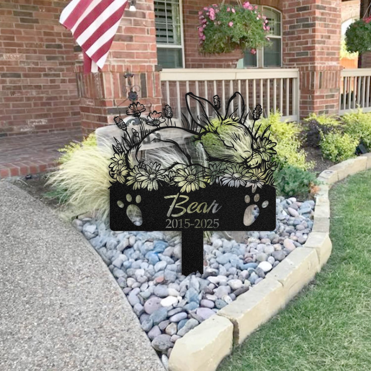 Bunny pet grave marker staged near a home entryway, showing the finished sleeping-pose daisy floral design and name plate outdoors.