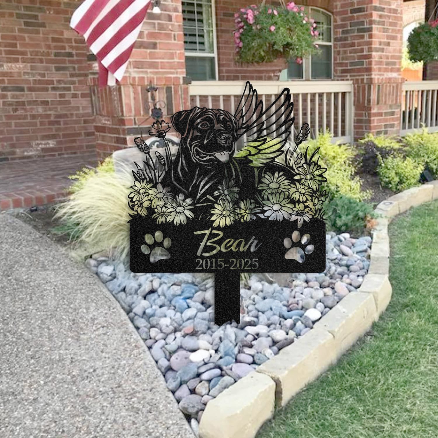 Cane Corso pet grave marker placed in a rock garden bed in front of a brick house porch with an American flag