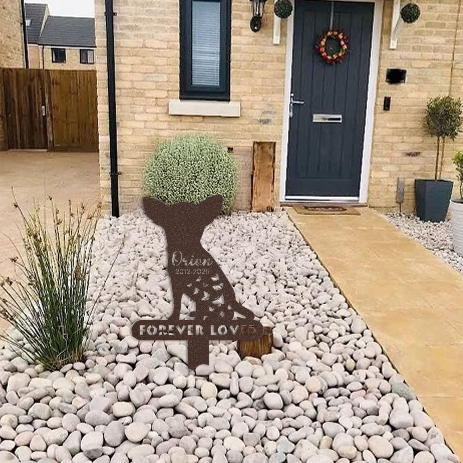 Chihuahua pet grave marker displayed among garden plants and stone edging, showing the butterfly silhouette design with the 'Forever Loved' engraving as an outdoor memorial accent.