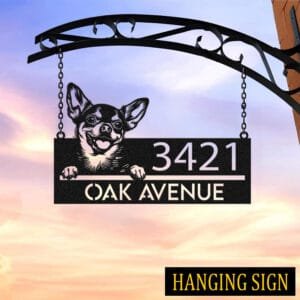 Personalized Chihuahua address sign hanging by chains from a wrought iron bracket against a sunset sky