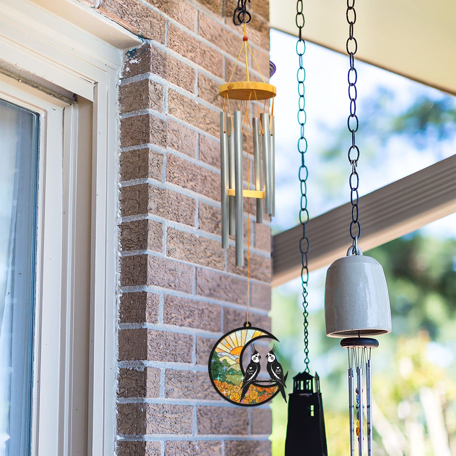 Cockatiel wind chime suncatcher hanging beside a brick wall and window next to other decorative bells and chimes