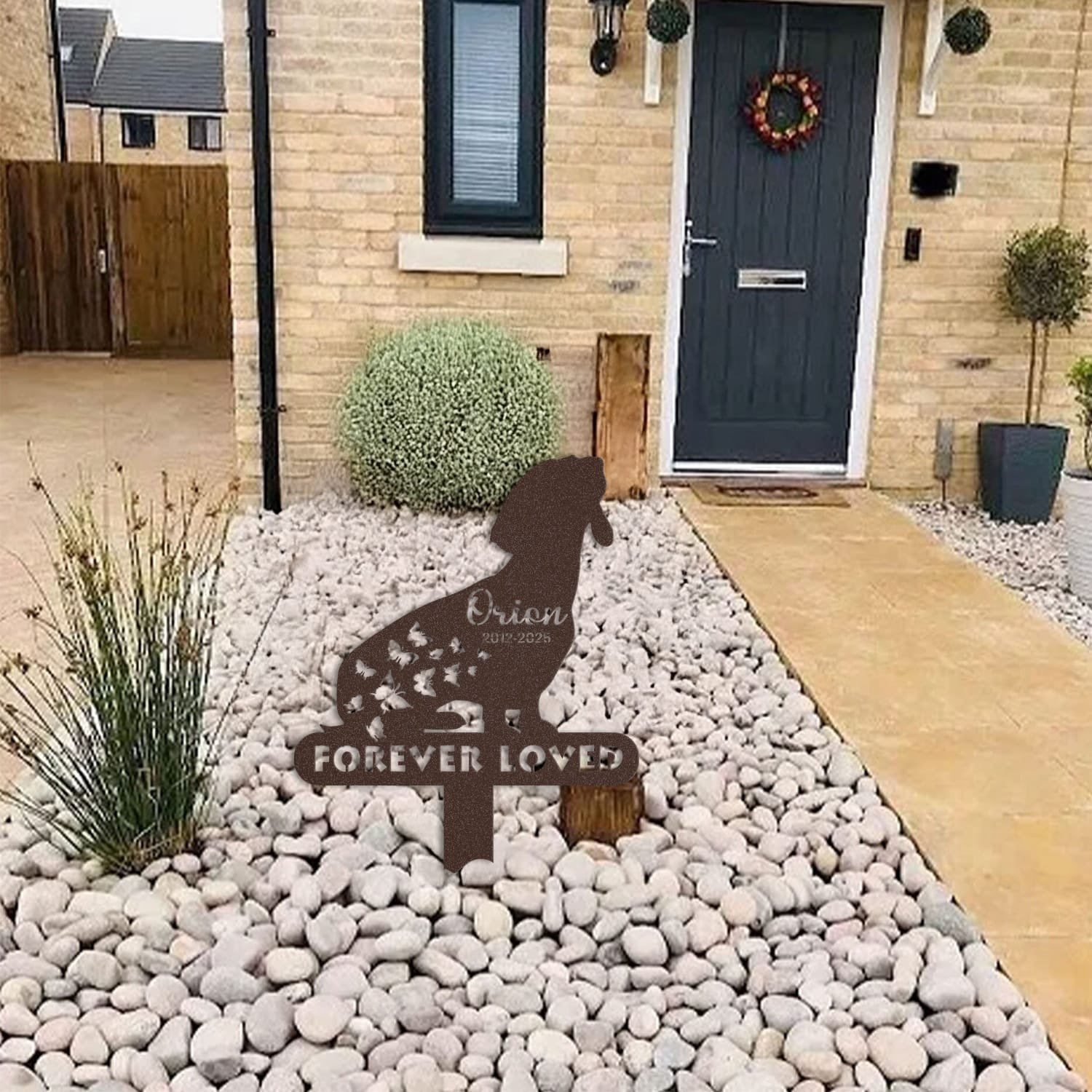 Dachshund pet grave marker displayed among garden plants and stone edging, showing the butterfly silhouette design with the 'Forever Loved' engraving as an outdoor memorial accent.