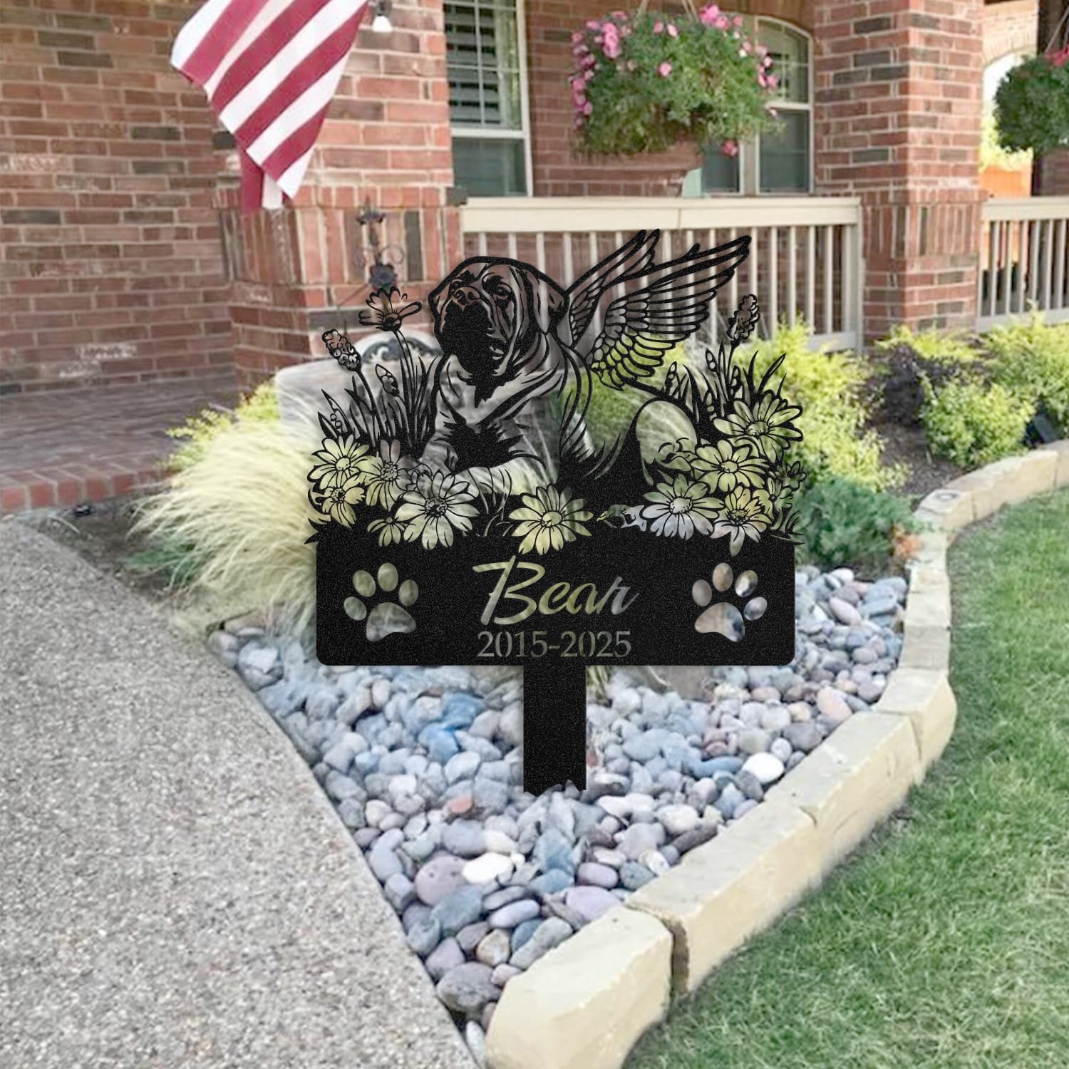 English Mastiff pet grave marker placed in a rock garden bed in front of a brick house porch with an American flag