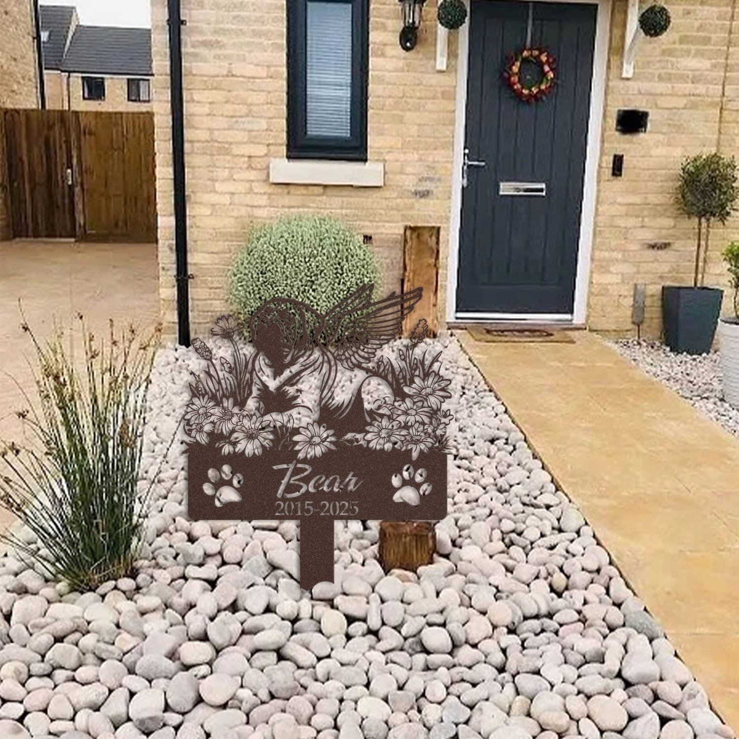 English Mastiff pet grave marker in a light stone garden bed outside a brick home with a blue front door and wreath