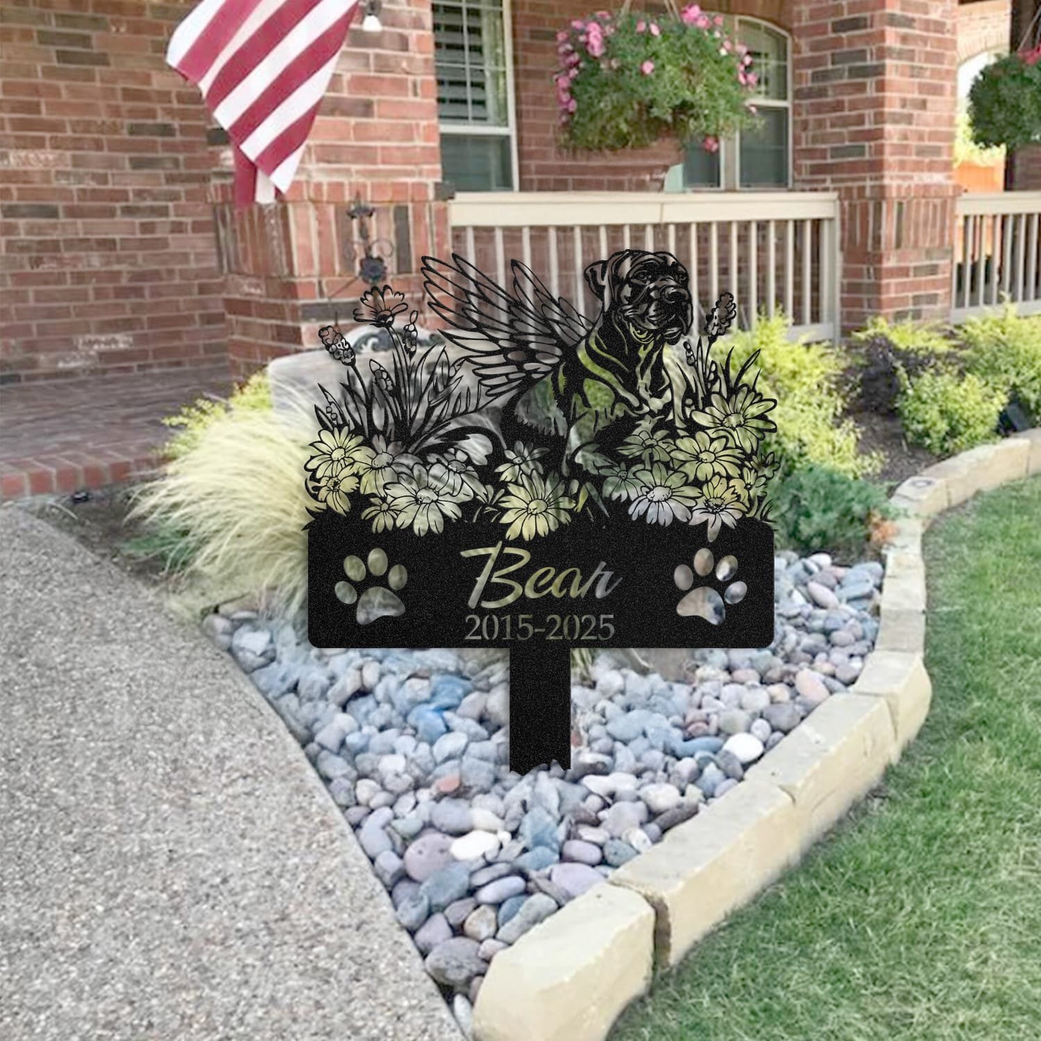 Great Dane pet grave marker placed in a rock garden bed in front of a brick house porch with an American flag