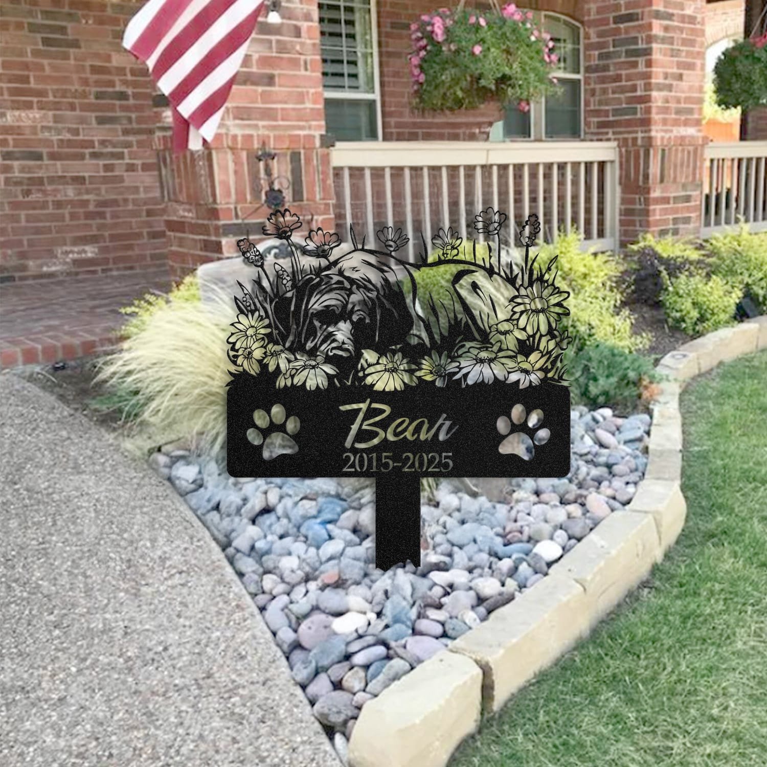 Great Dane pet grave marker placed in a rock garden bed in front of a brick house porch with an American flag