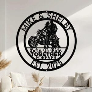 Metal wall art design of a couple in riding gear standing together beside a cruiser motorcycle, set within a circular frame reading the couple's names at the top and 'Born To Ride Together Forever' with the established year at the bottom, fully personalizable.