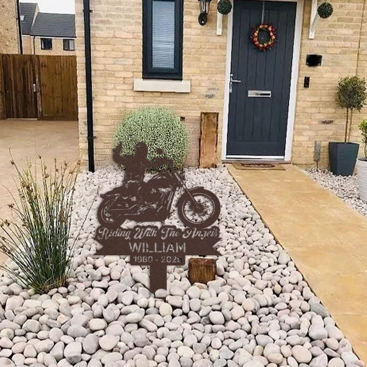 Motorcycle human grave marker displayed among garden plants and stone edging, showing the motorcycle rider silhouette design as an outdoor memorial accent.