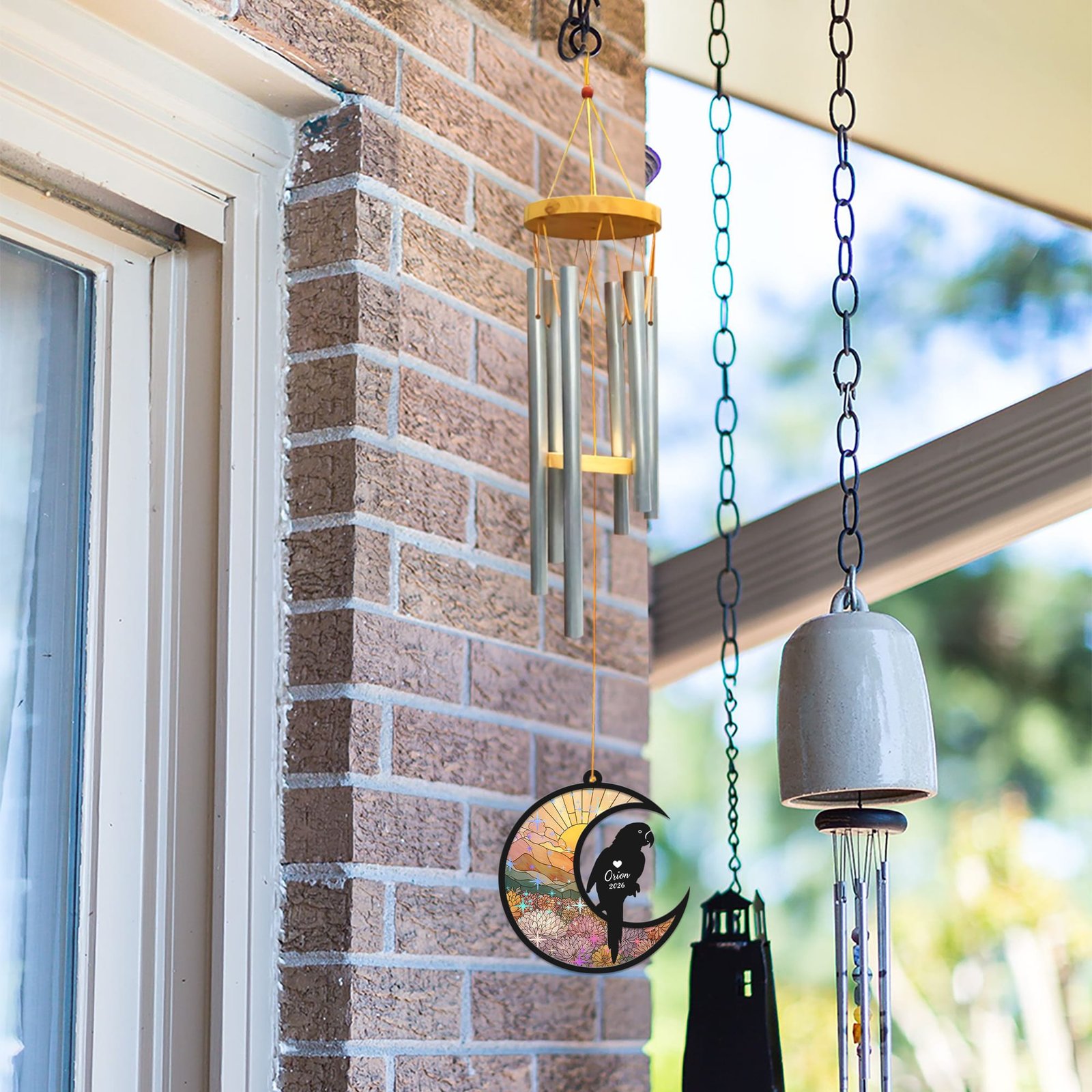 Parrot wind chime suncatcher hanging beside a brick wall and window next to other decorative bells and chimes