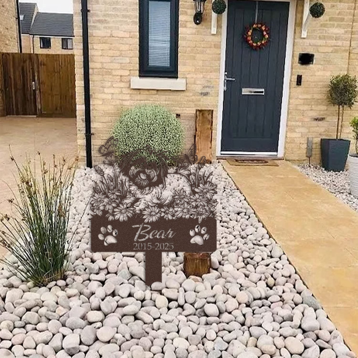 Shih Tzu pet grave marker displayed among garden plants and stone edging, showing the daisy garden design with butterflies as an outdoor memorial accent.