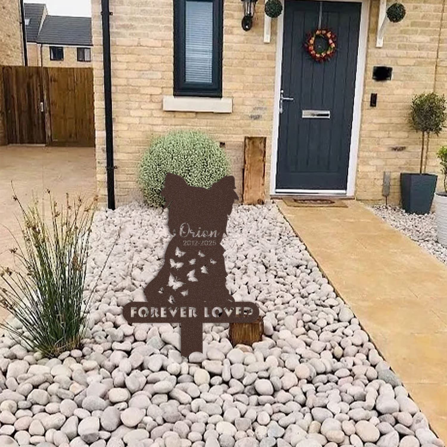 Yorkshire Terrier pet grave marker displayed among garden plants and stone edging, showing the two-pet silhouette design with the 'Forever Loved' engraving as an outdoor memorial accent.